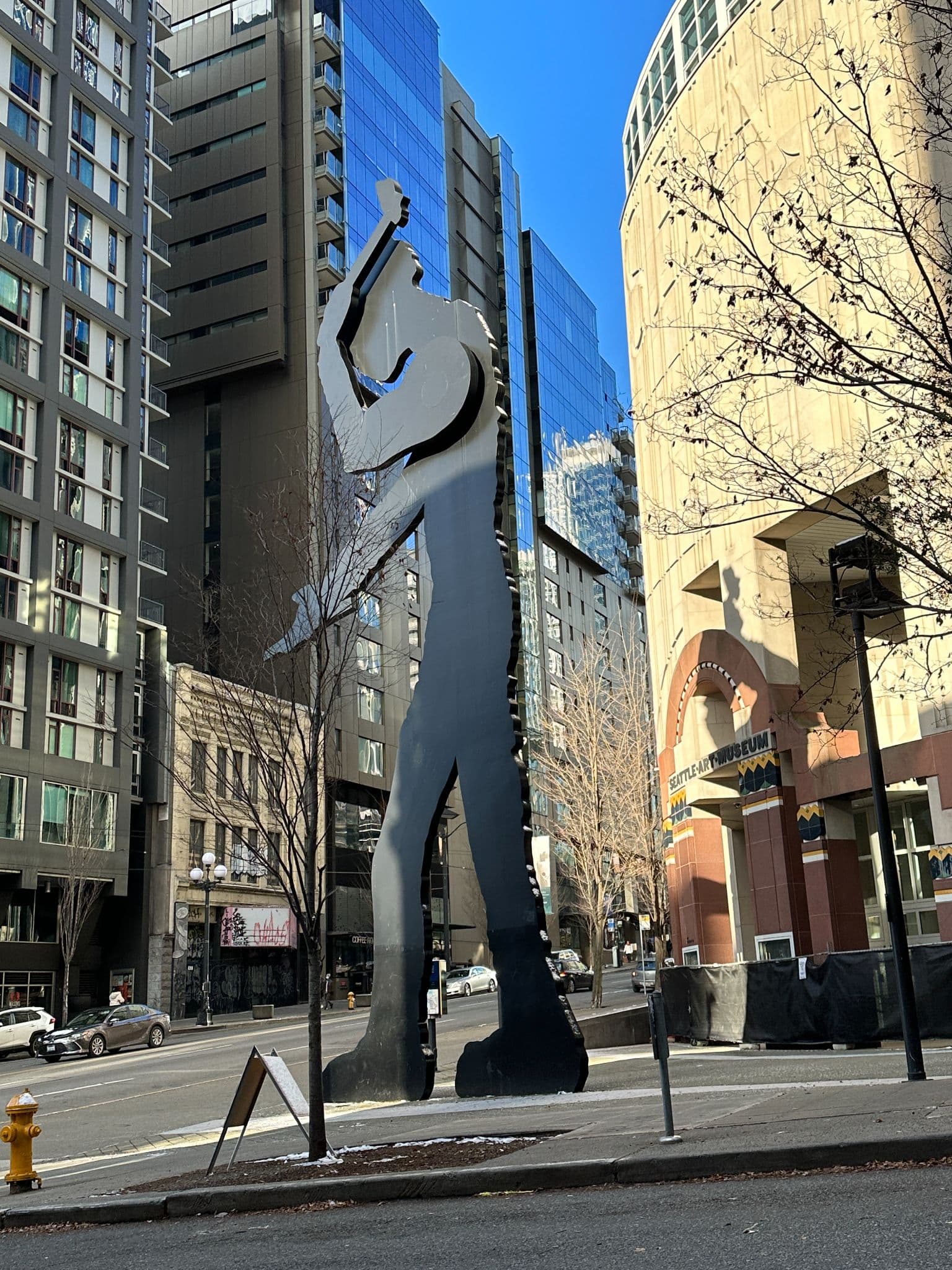 A Seattle street view: Borofsky's Hammering Man sculpture in front of the Seattle Art Museum, with the Lusty Lady building visible across the street and the downtown skyline behind