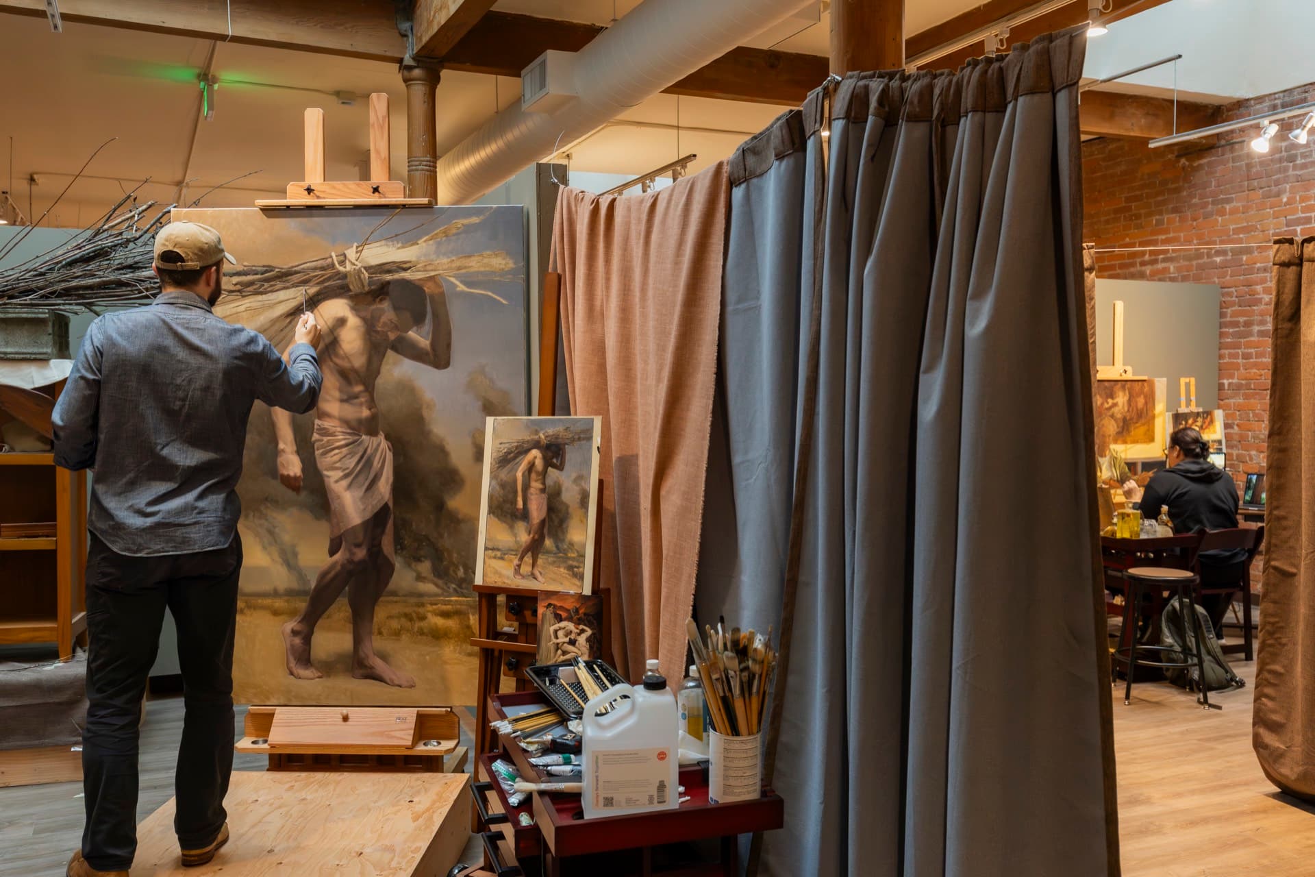 A painter working on a large figure painting next to a curtained studio bay during a workshop on the Occidental third floor.